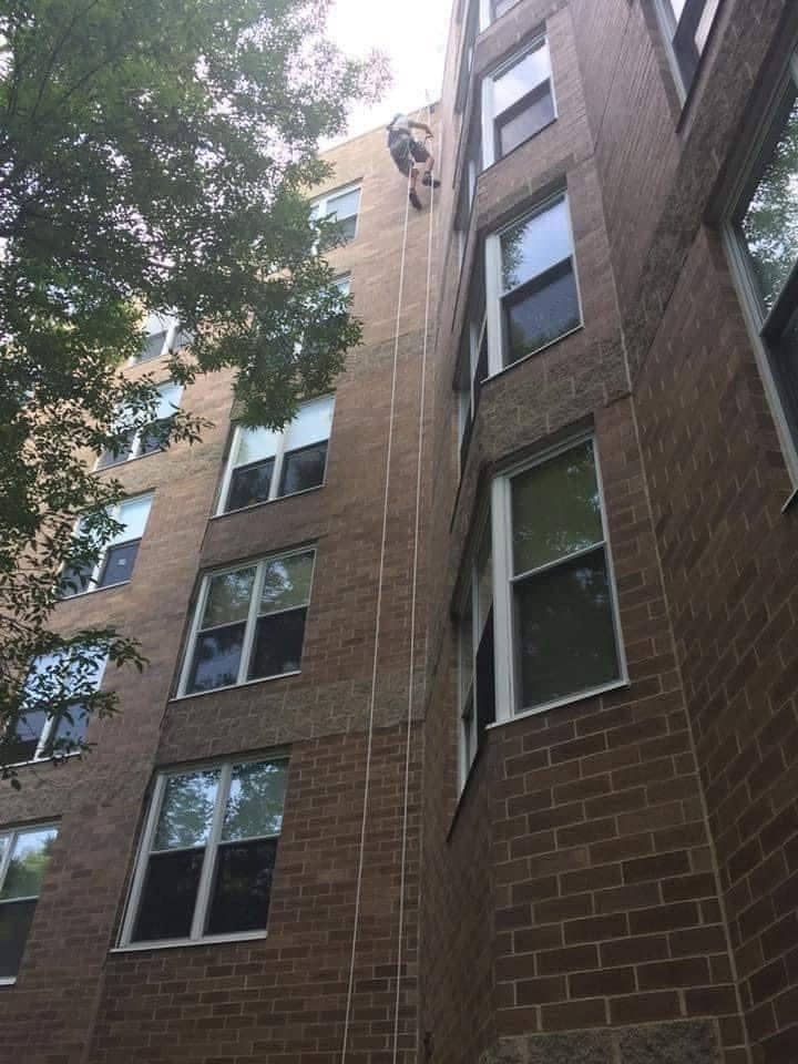 Technician on rope access at the top of a four-story brick apartment building